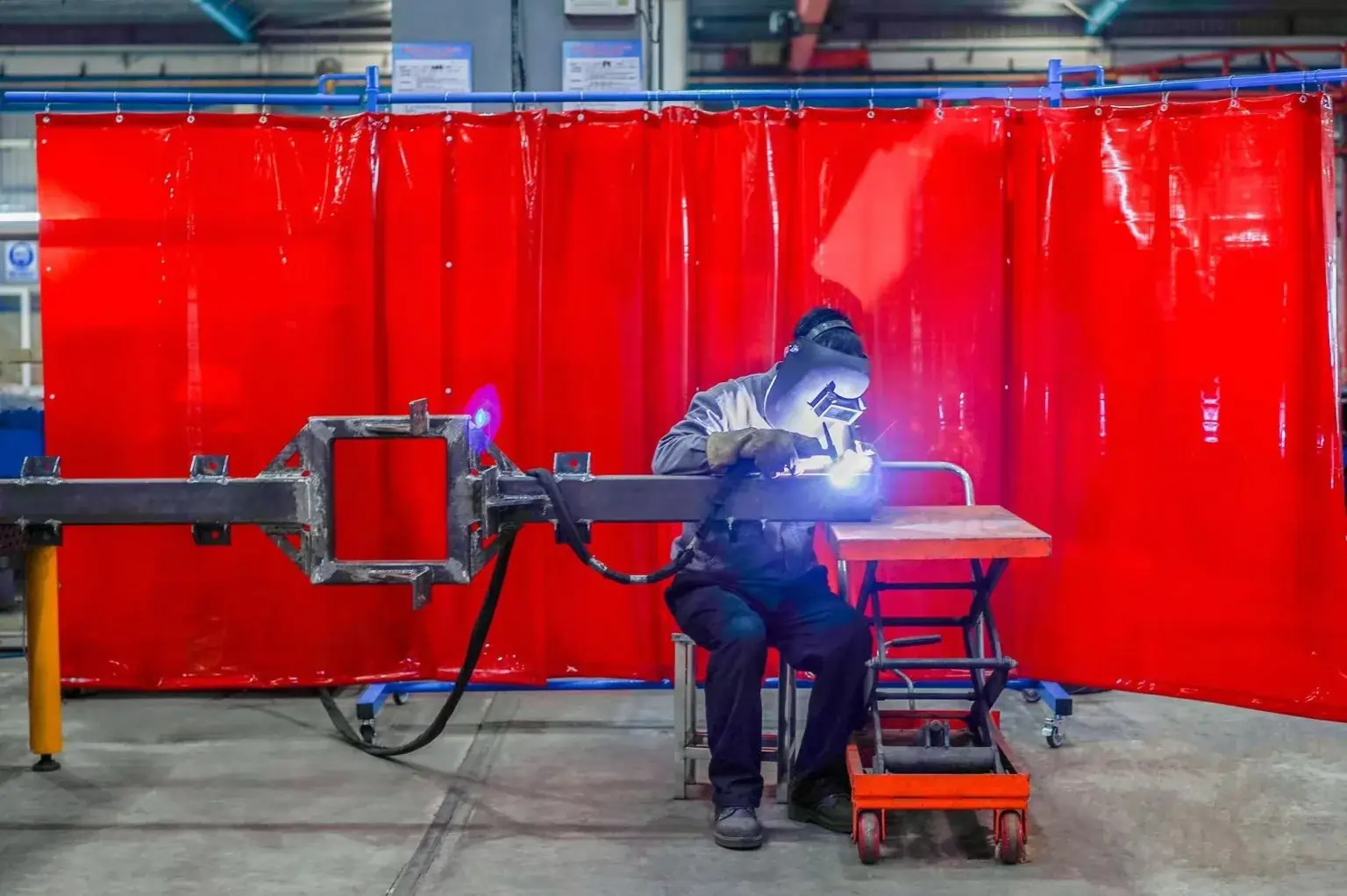 A man welding with PVC welding curtains in the background as protection