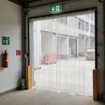 Fire retardant PVC strip curtains in a warehouse doorway with fire escape sign above the doorway and a fire extinguisher