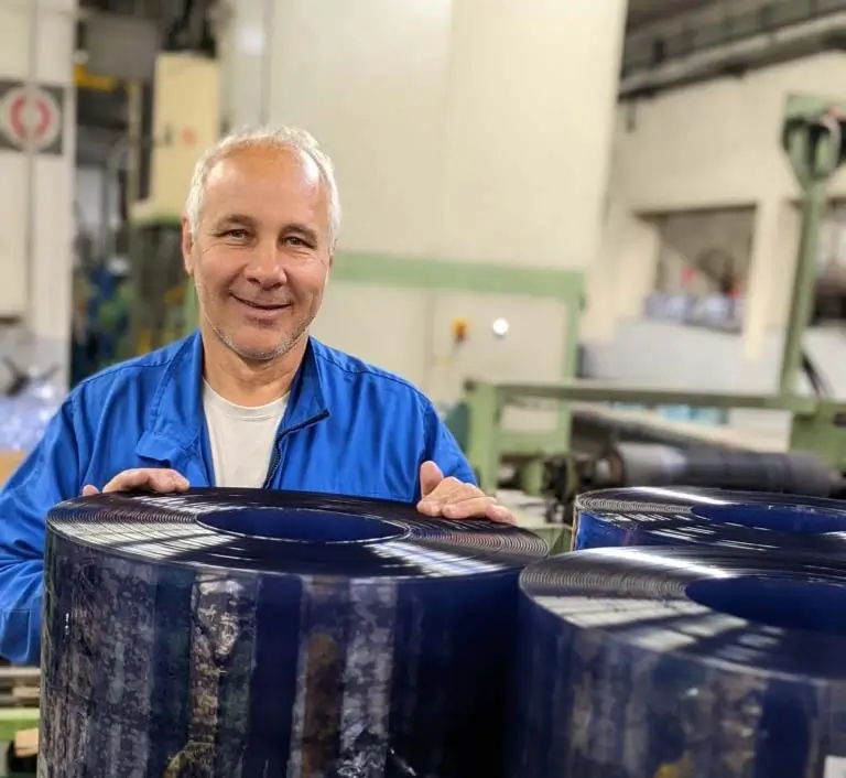 Warehouse worker standing behind PVC rolls and smiling