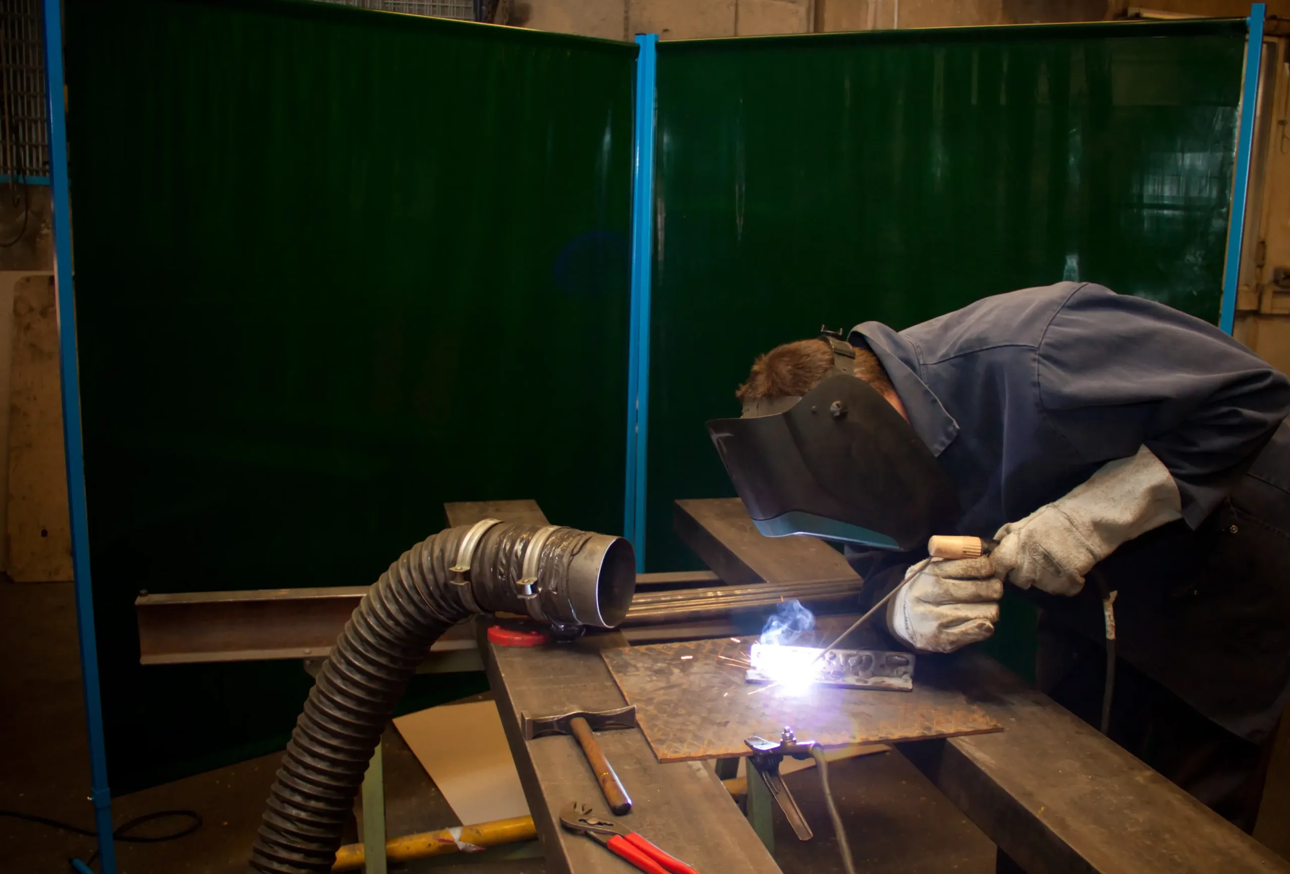 Man welding with green screenlex welding screens behind him